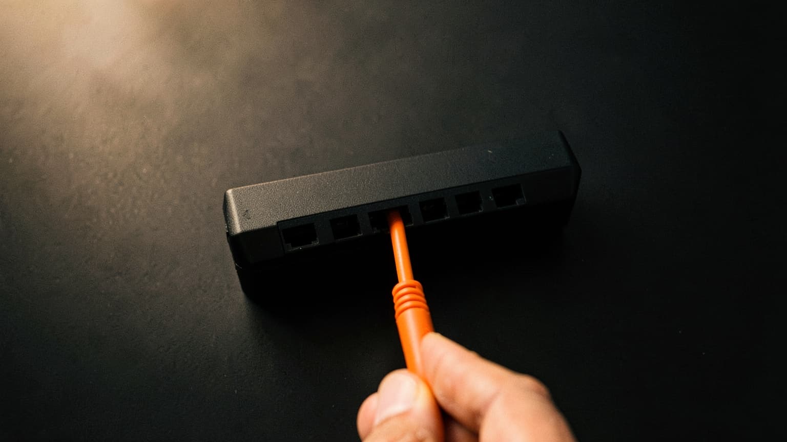 A hand holding one orange network cable beside a black switch with a single empty port